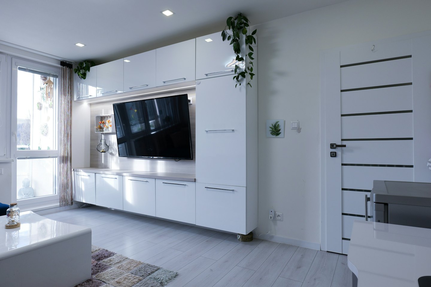 Moderner weißer Fernsehschrank mit hängenden grünen Pflanzen.